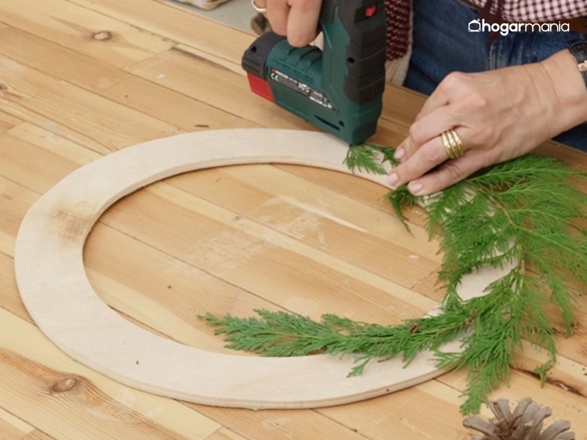 Comienza fijando las ramas una a una para cubrir el aro de madera con un primer tramo verde.