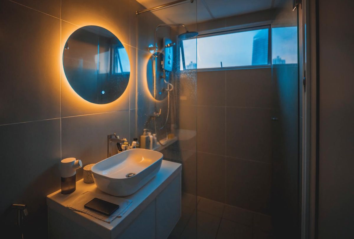 Baño con espejo redondo con iluminación integrada.