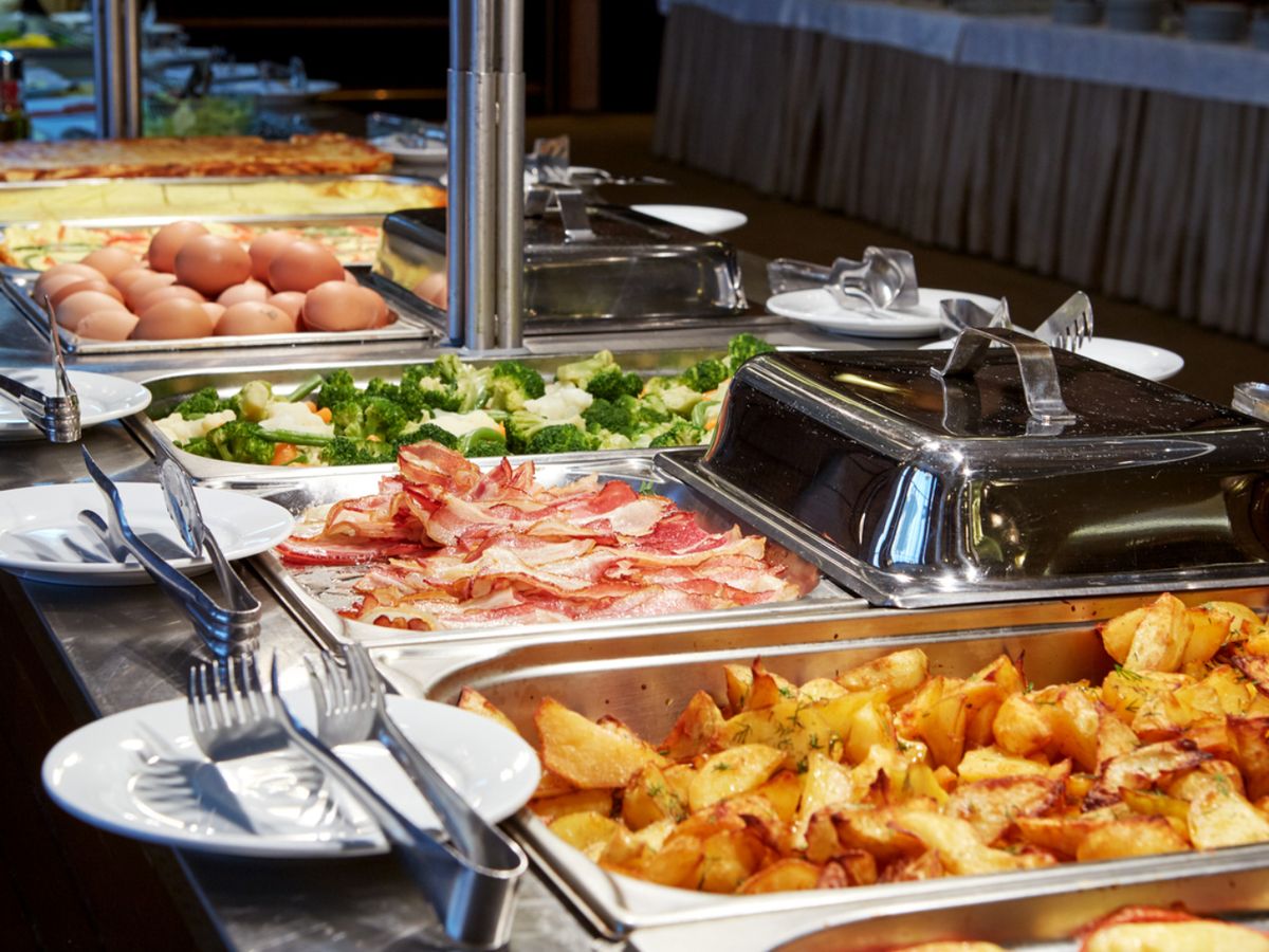 Un desayuno buffet en hotel con opciones calientes: bacon, patatas, huevos y verduras.