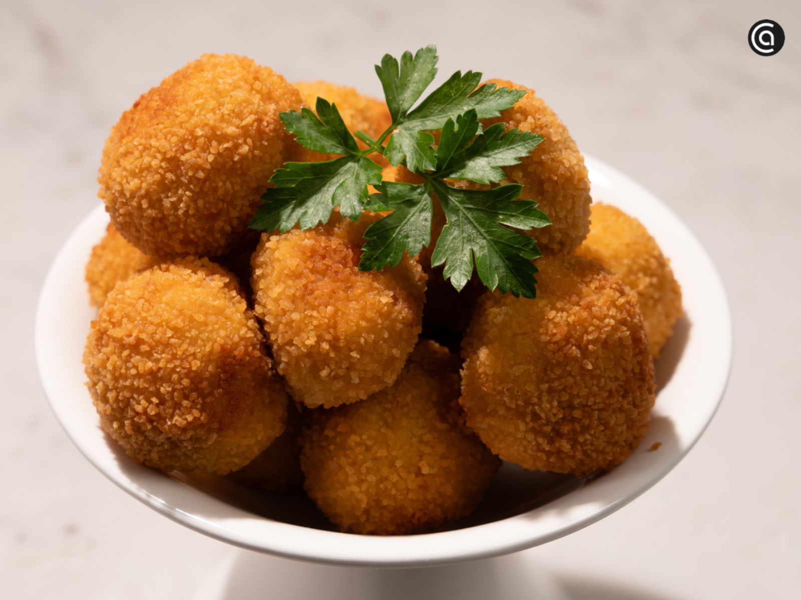 Croquetas de txangurro doradas y crujientes, coronadas con perejil fresco y listas para disfrutar en un bocado.