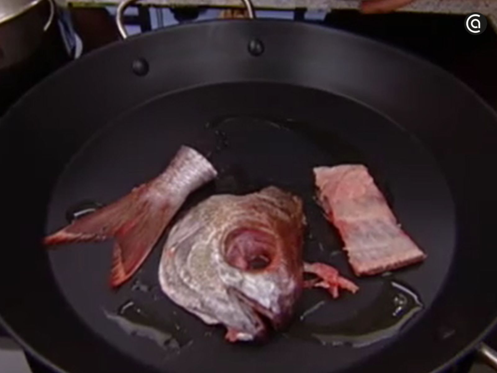Cabeza, espinas y cola del besugo dorándose suavemente en la sartén para extraer todo su sabor.