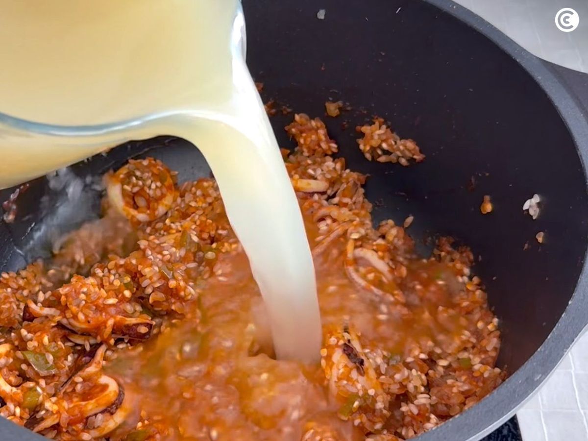 Cubrir el arroz con caldo para hacerlo caldoso con marisco