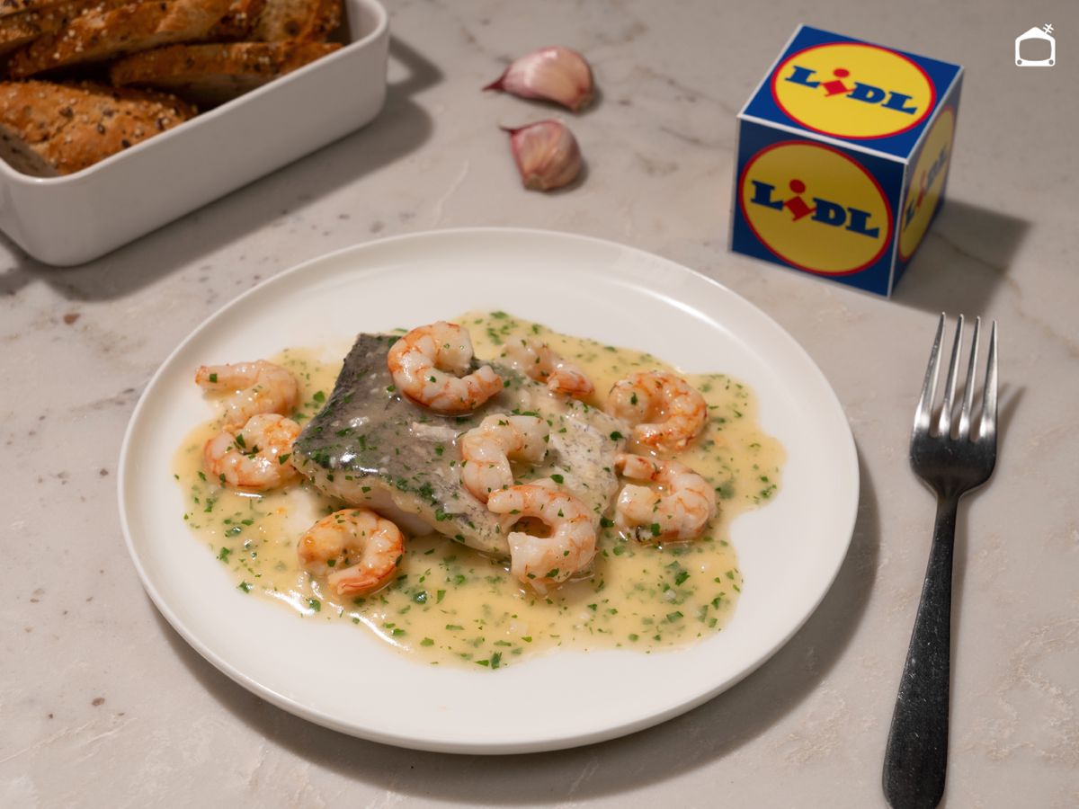 Un plato de merluza jugosa con gambas y salsa suave, listo para llevar a la mesa y acompañar con un buen pan.