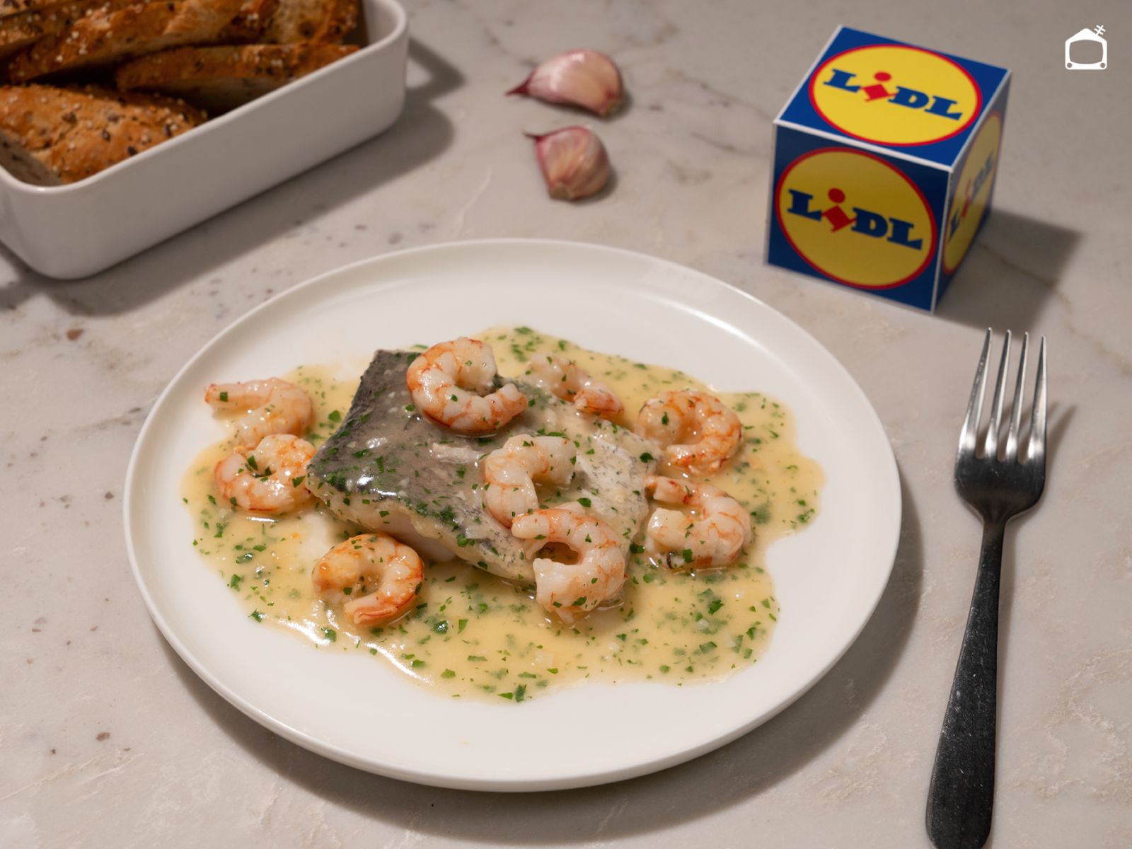 Un plato de merluza jugosa con gambas y salsa suave, listo para llevar a la mesa y acompañar con un buen pan.