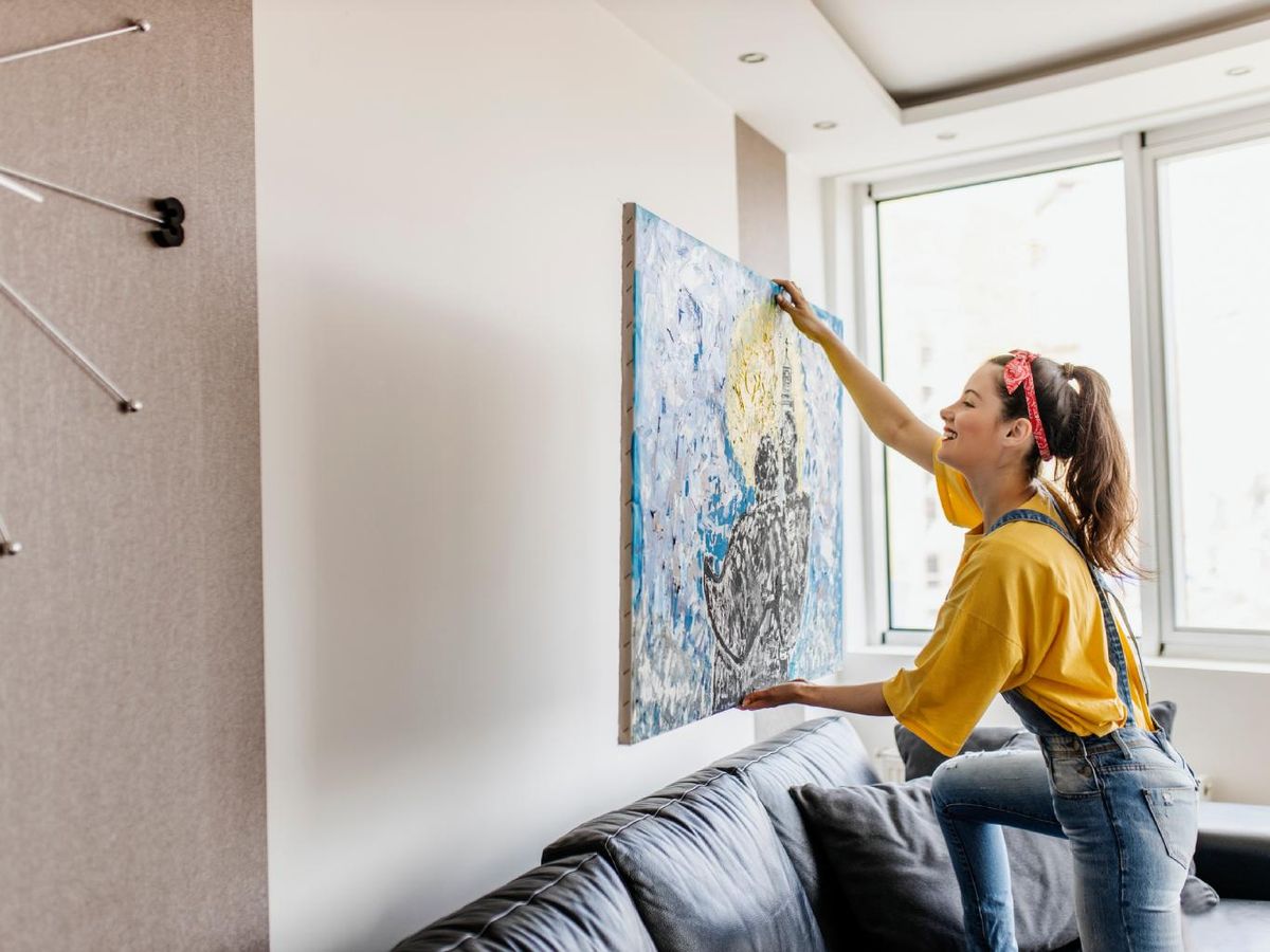 ujer colocando un cuadro encima del sofá.