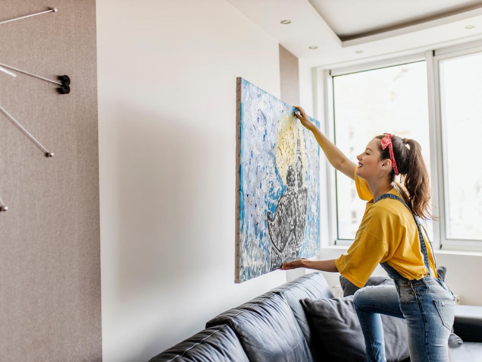 ujer colocando un cuadro encima del sofá.