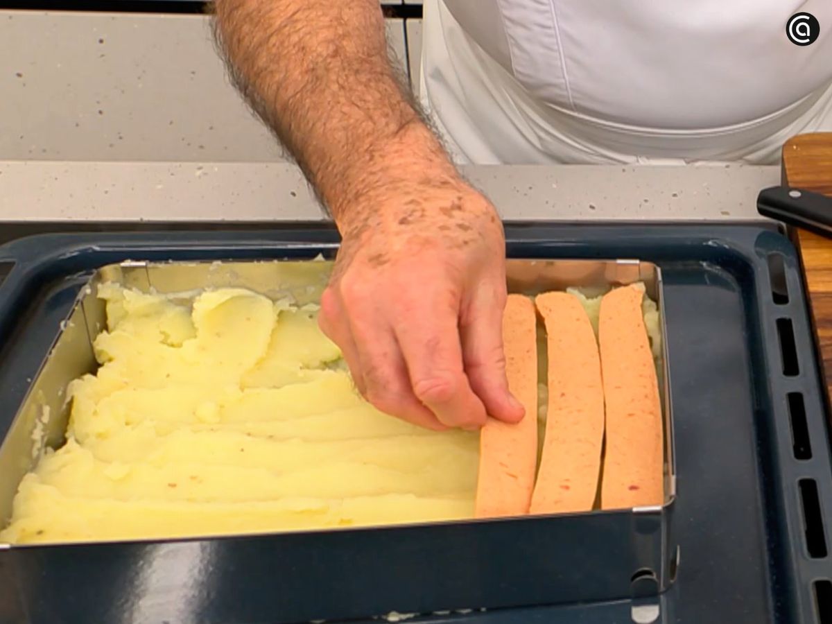 Haz una cama de puré en la bandeja y coloca las salchichas encima