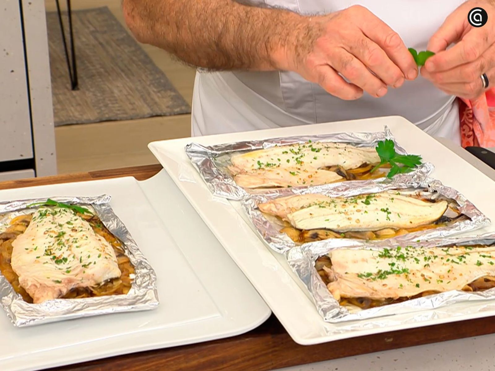 Abre el papillote, sirve la lubina con champiñones y decora con unas hojas de perejil