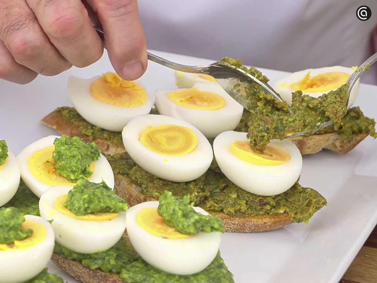 Tuesta el pan en el horno, unta con el pesto y coloca las mitades de huevo