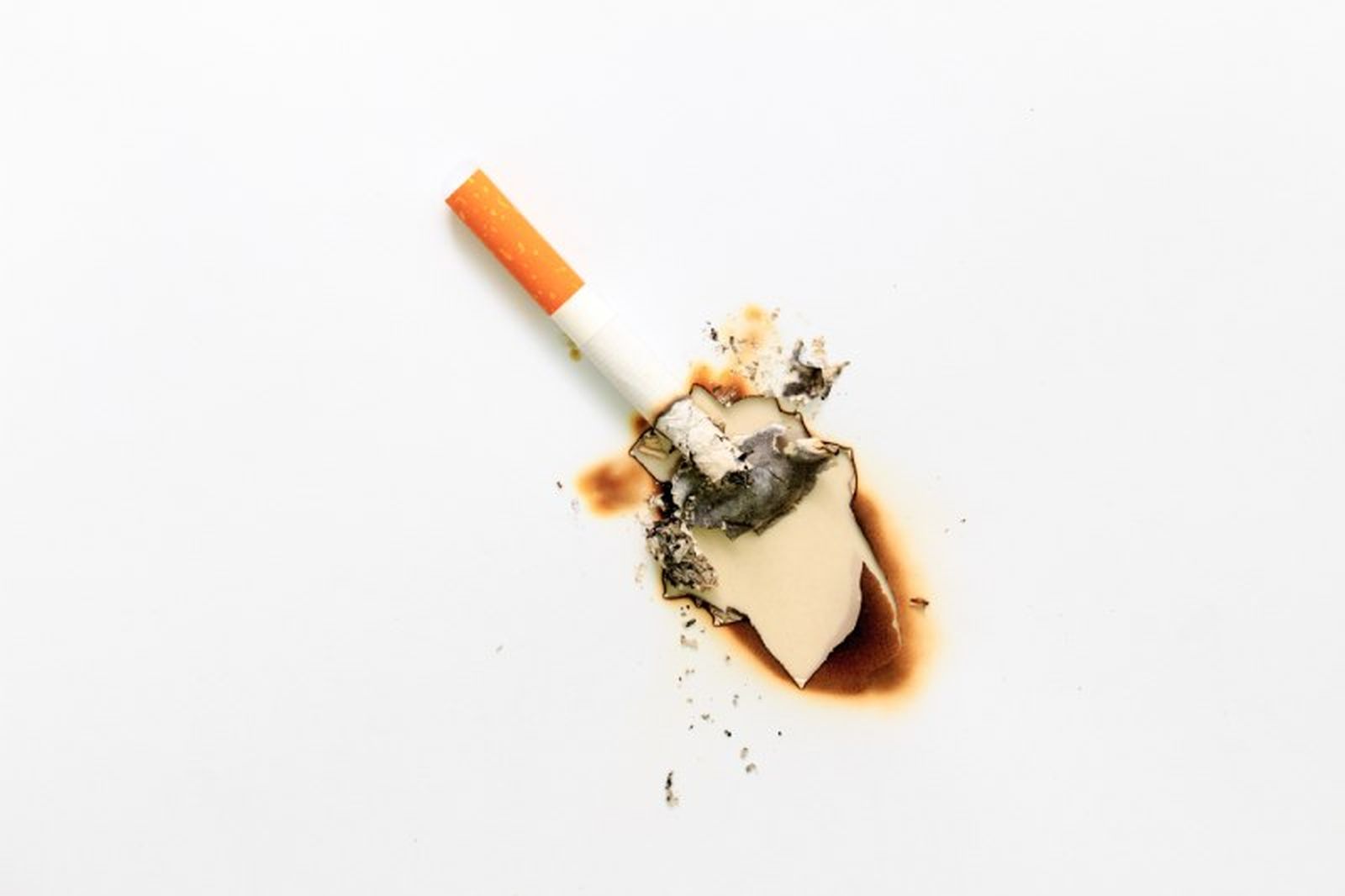 Cigarrillo quemando una superficie blanca de madera