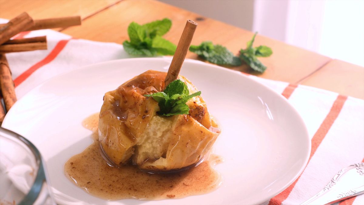 Decora las manzanas asadas con una ramita de canela y una hoja de menta, y vierte el jugo del asado por encima para un toque final que realza su presentación y sabor