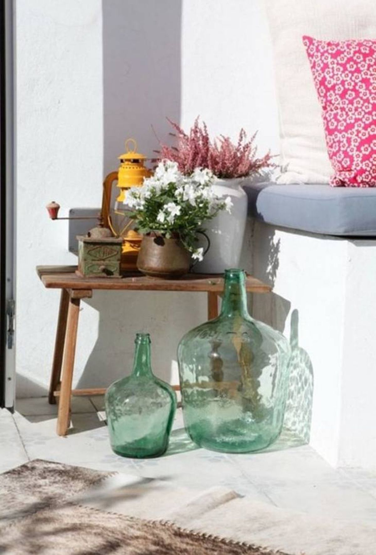 Patio exterior decorado con dos damajuanas verdes de diferente tamaño.