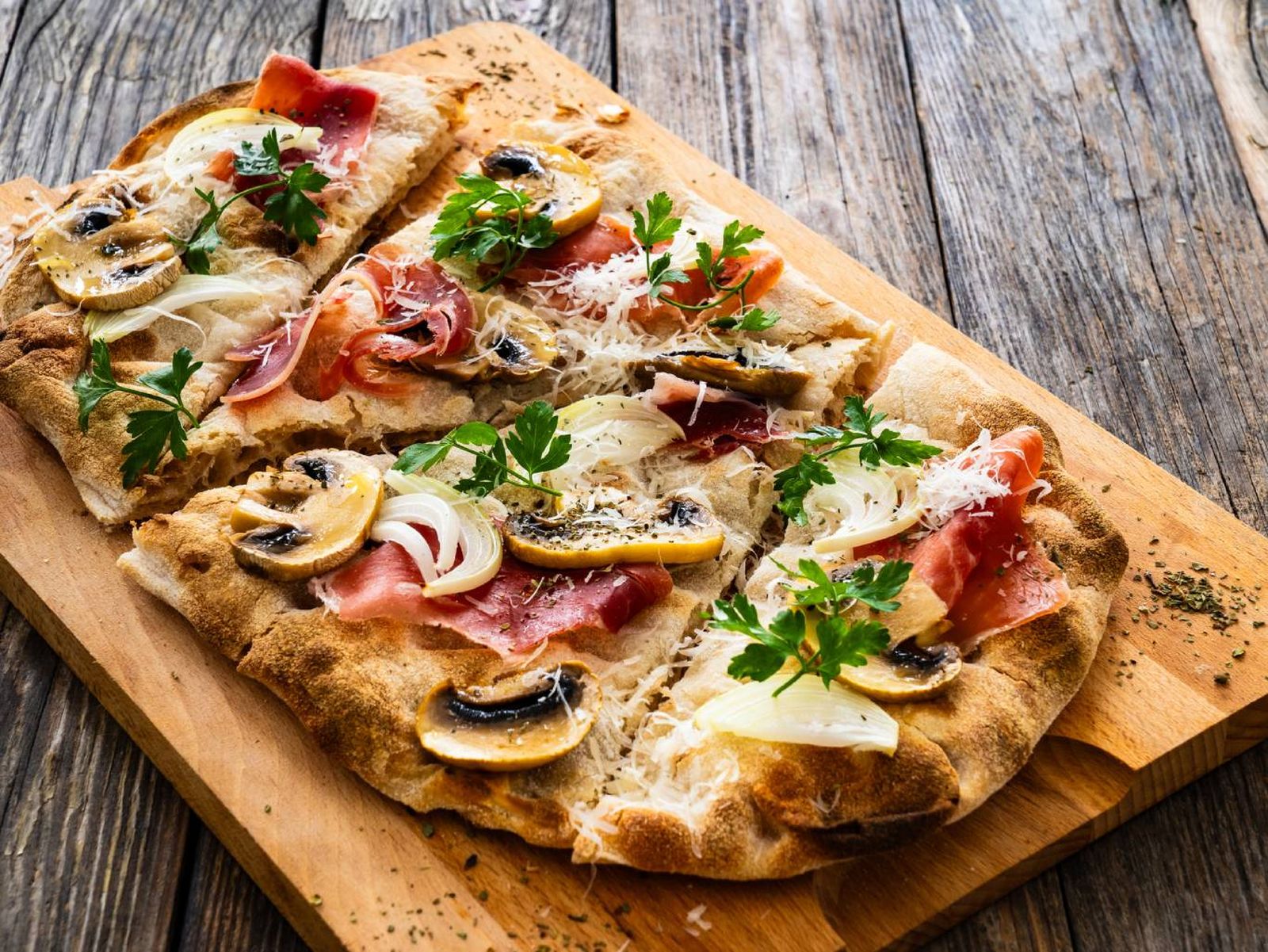La pizza romana se sirve en porciones rectangulares con una base crujiente y coberturas variadas.