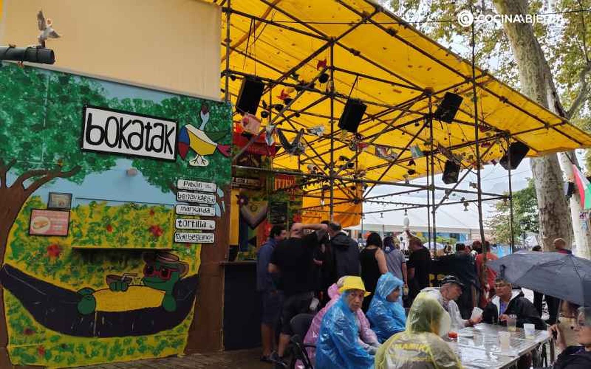 Varias personas disfrutan, a pesar de la lluvia, de una comida en la txosna Sinkuartel