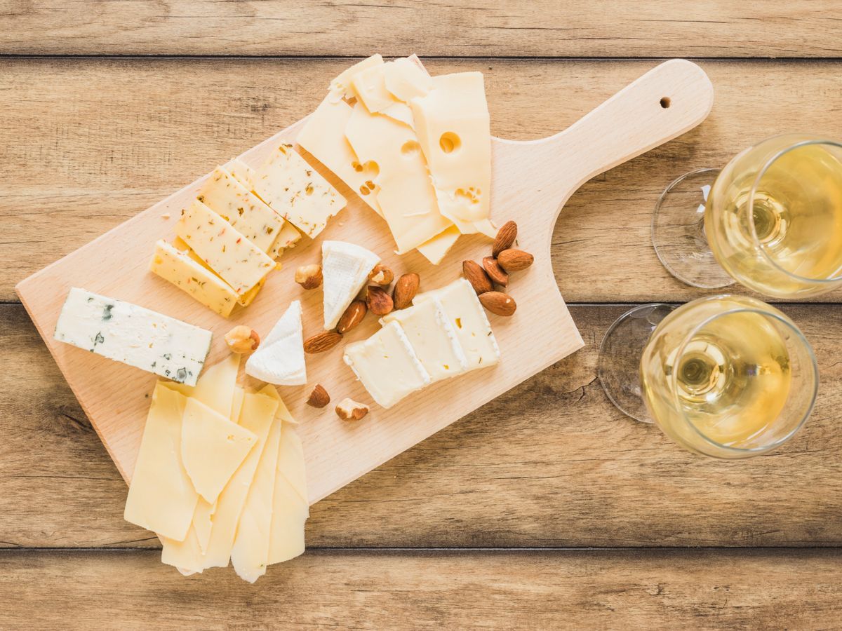 Tabla de quesos variados con almendras y vino blanco: combina texturas suaves y curadas para un maridaje elegante.