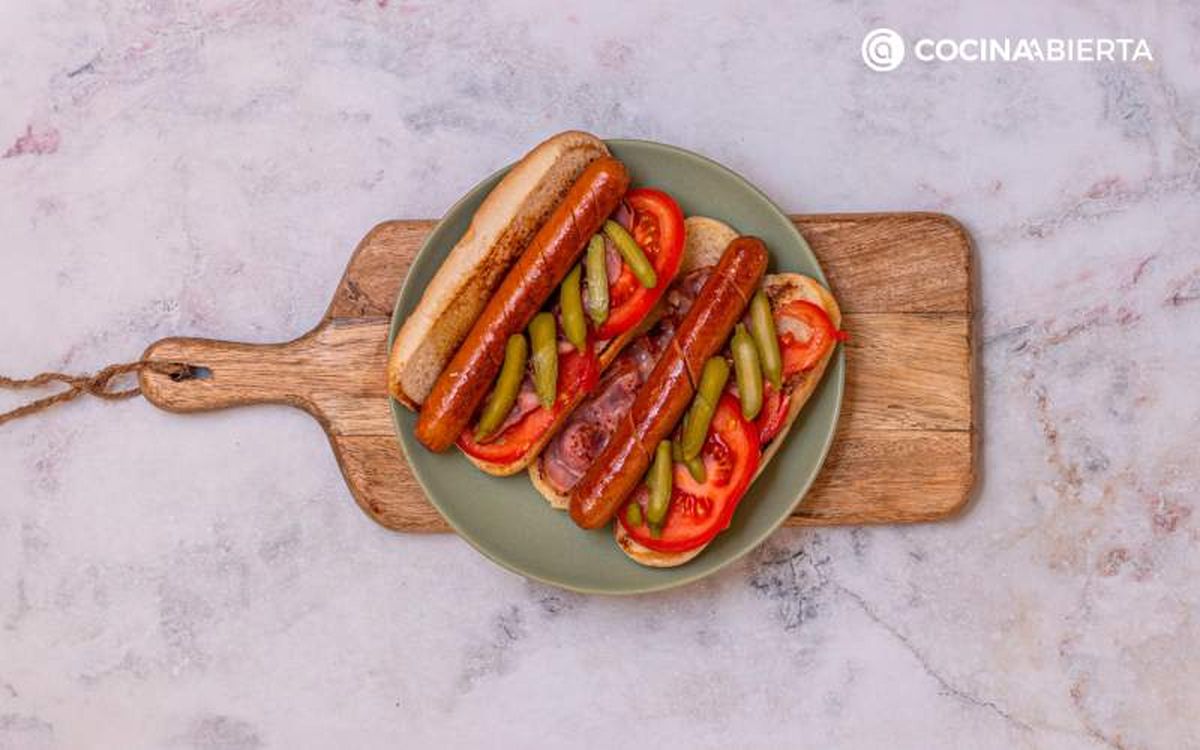Pon la salchicha, el tomate, el bacon y los pepinillos en el bollo