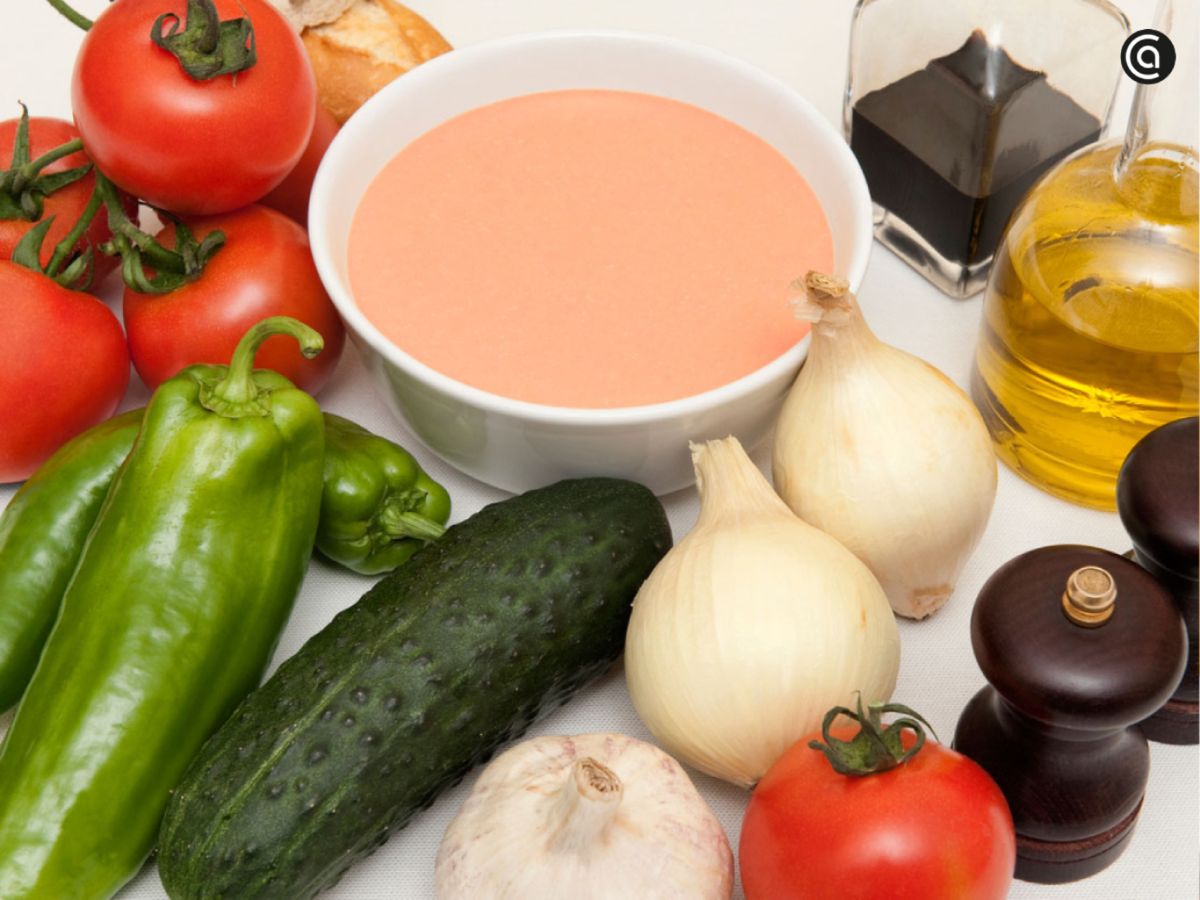 Gazpacho andaluz acompañado de sus ingredientes frescos: tomate, pimiento, pepino, ajo, cebolla, aceite de oliva y vinagre.