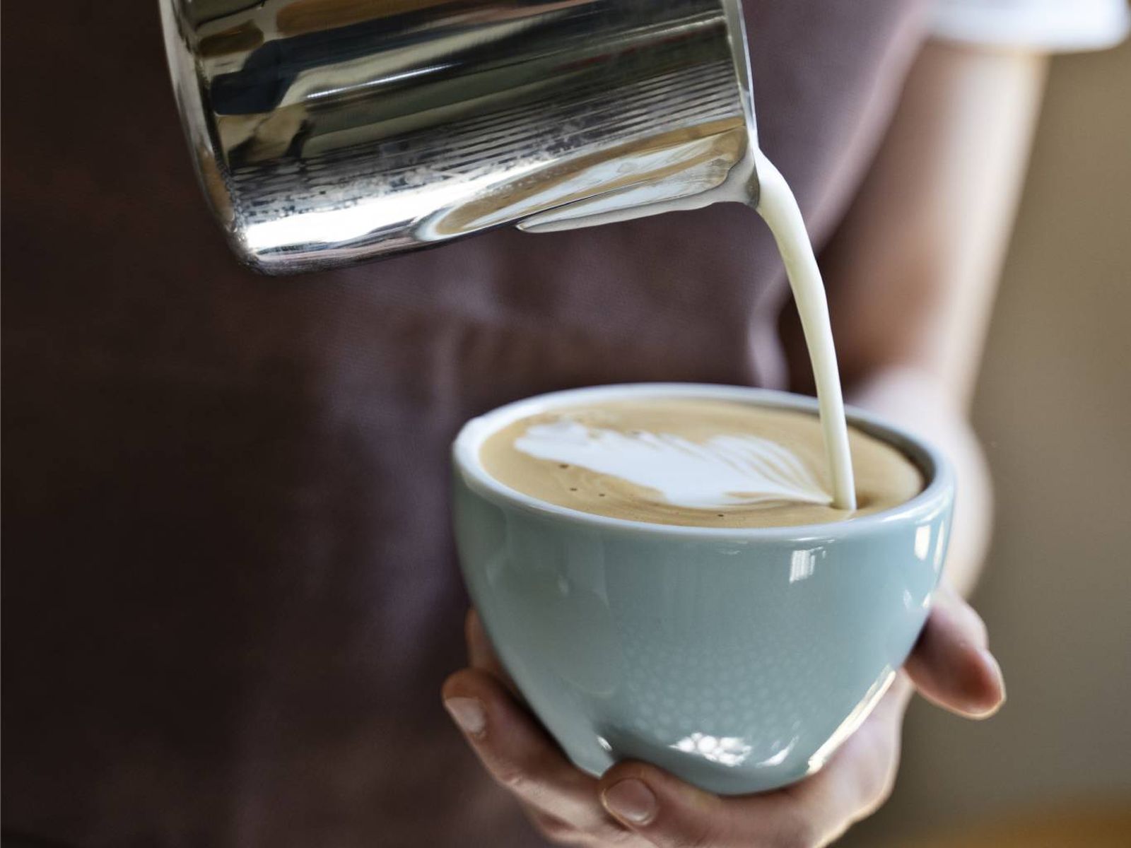 Un barista vierte la leche sobre el espresso para crear un flat white con un delicado dibujo. Un barista vierte la leche sobre el espresso para crear un flat white con un delicado dibujo.