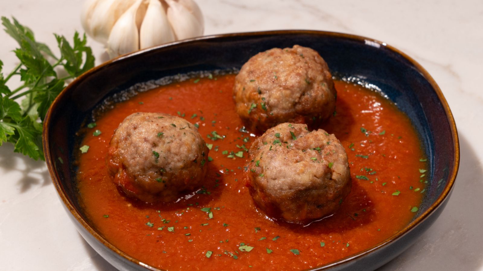 Albóndigas jugosas de ternera servidas con salsa de tomate y un toque de perejil.