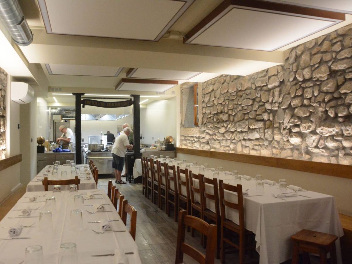 Interior de una sociedad gastronómica: cocina abierta al fondo y largas mesas preparadas para la comida.