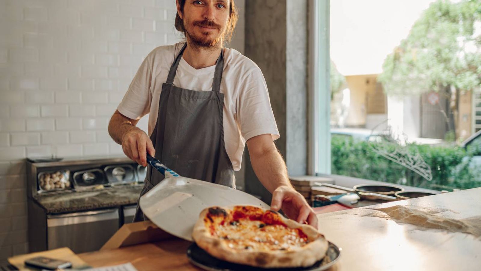 Un pizzero saca del horno una pizza recién hecha, lista para servir.