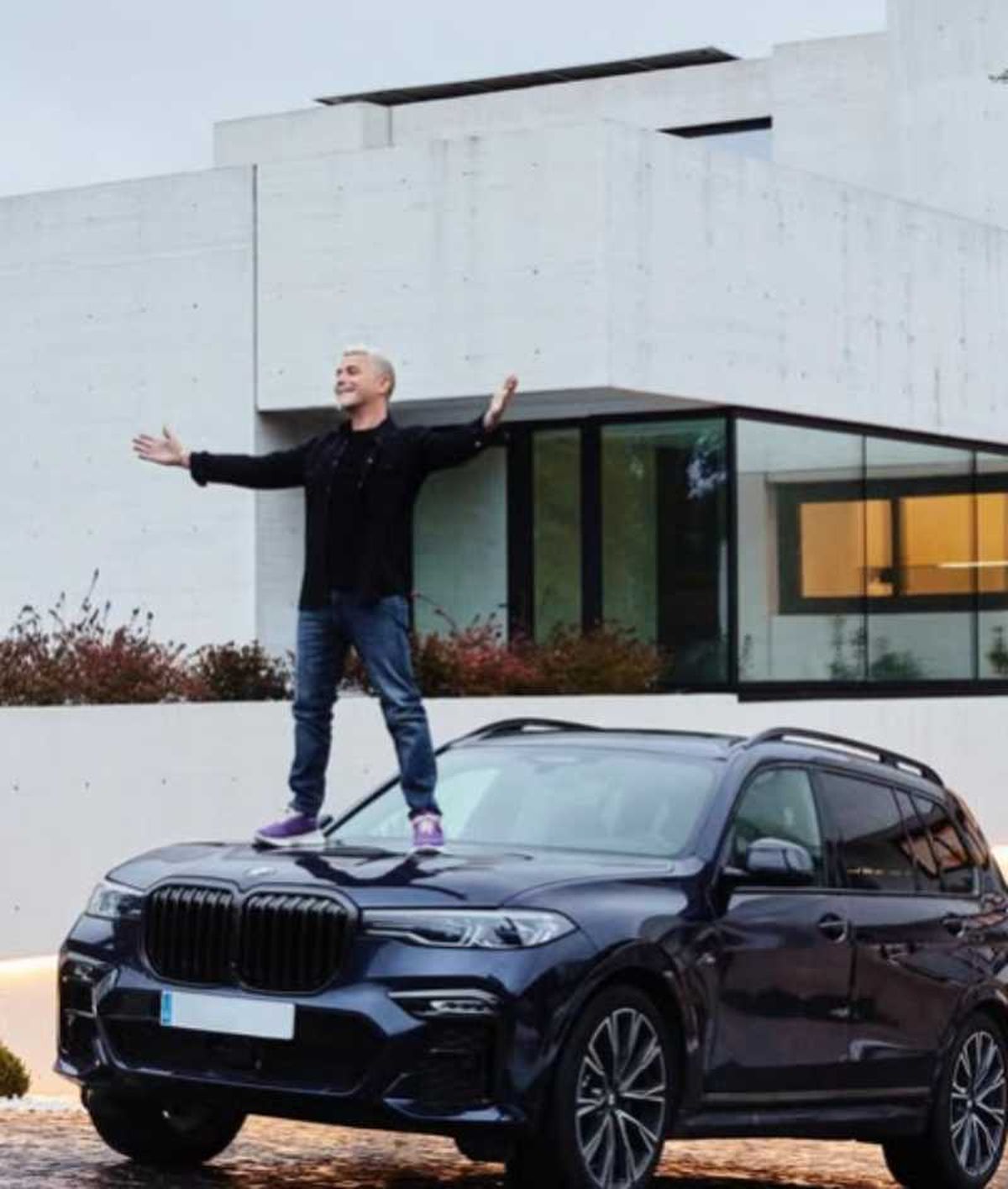 Alejandro Sanz subido en su coche con su hogar de fondo.