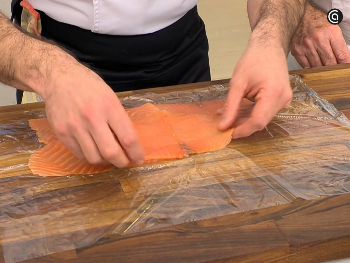 Las lonchas de salmón ahumado se disponen superpuestas sobre film para formar la base del rollo.