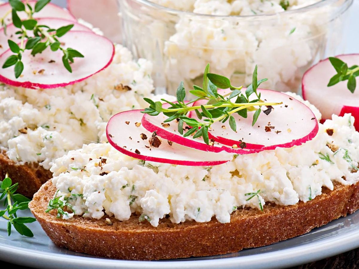 Tostada de pan integral con queso cottage, rábanos y hierbas frescas, una opción saludable y rápida para el desayuno.