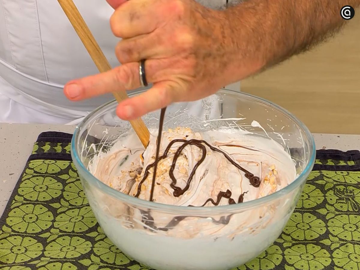 Agrega hilos de chocolate fundido y avellanas troceadas al merengue