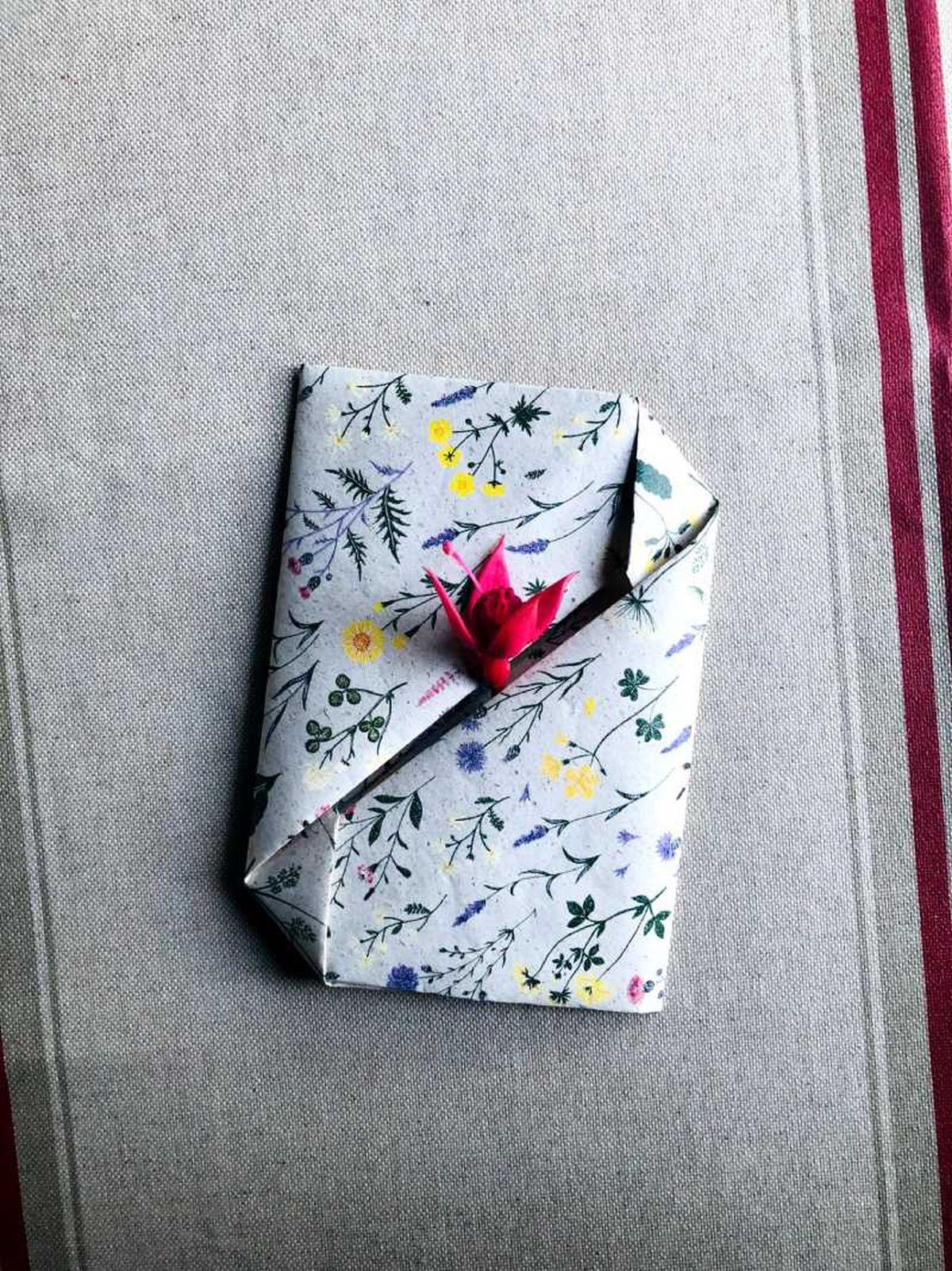 Sobre de papel floral decorado con una florecilla rosa.