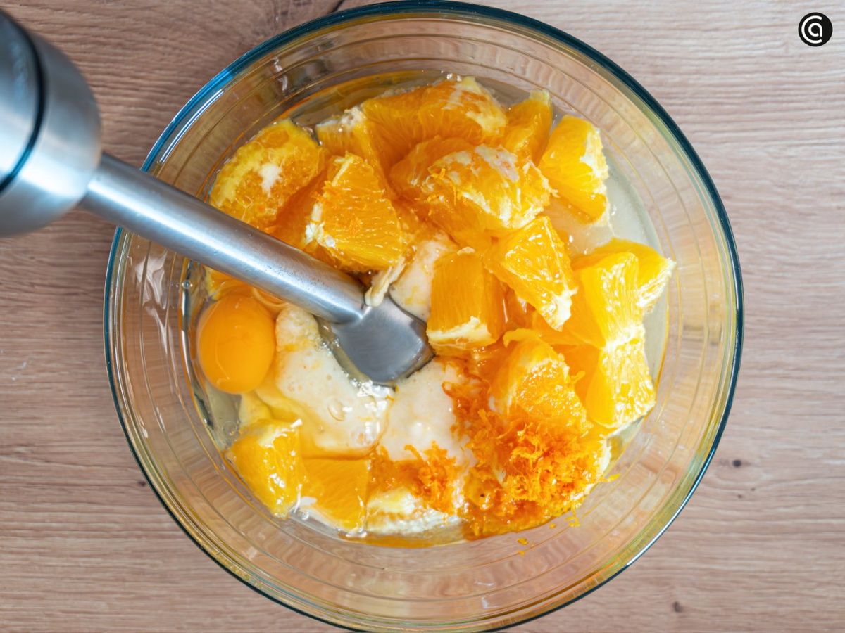 Tritura la naranja y mézclala con yogur, aceite, azúcar y huevos hasta obtener una crema homogénea