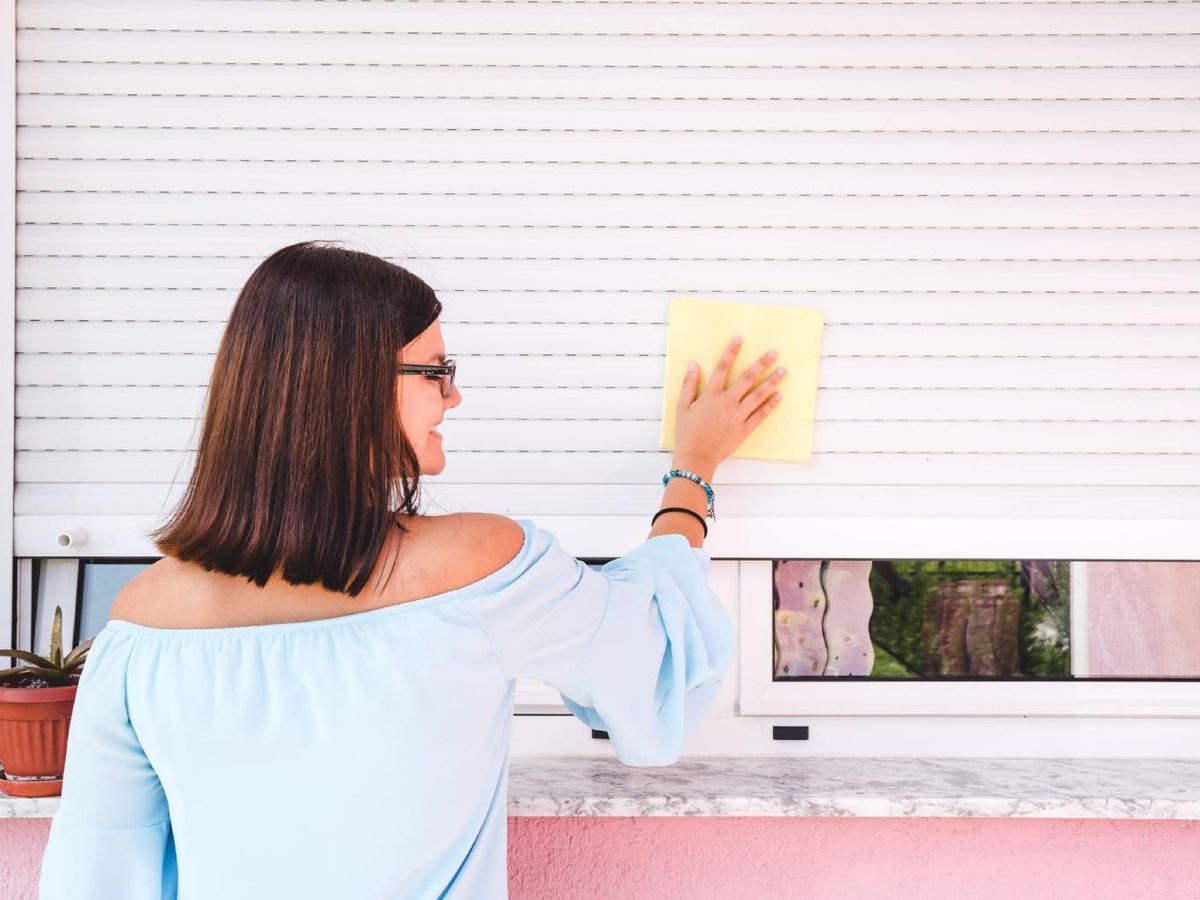 Mujer sonriente limpiando la persiana.