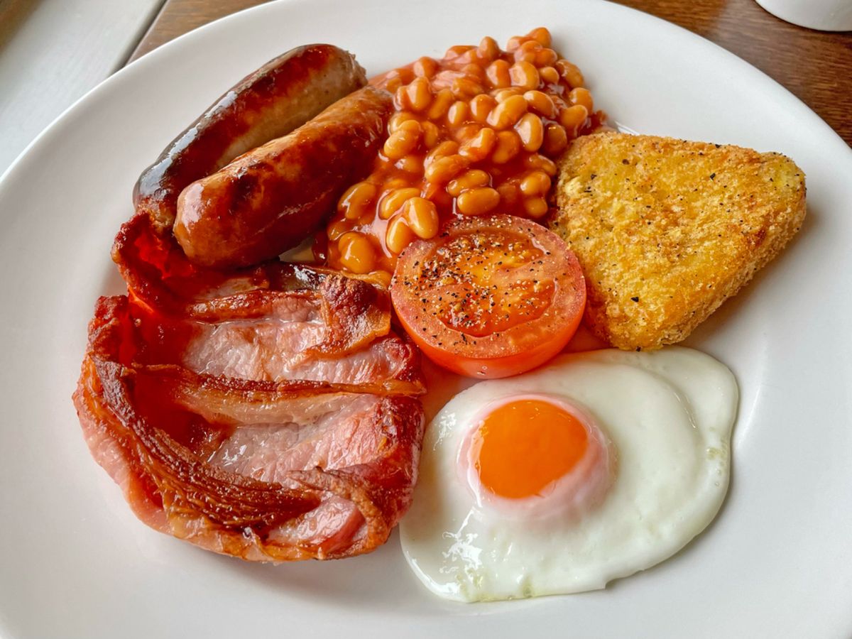 El clásico desayuno inglés con huevo, bacon, salchichas, alubias, tomate y hash brown servido en hotel británico.