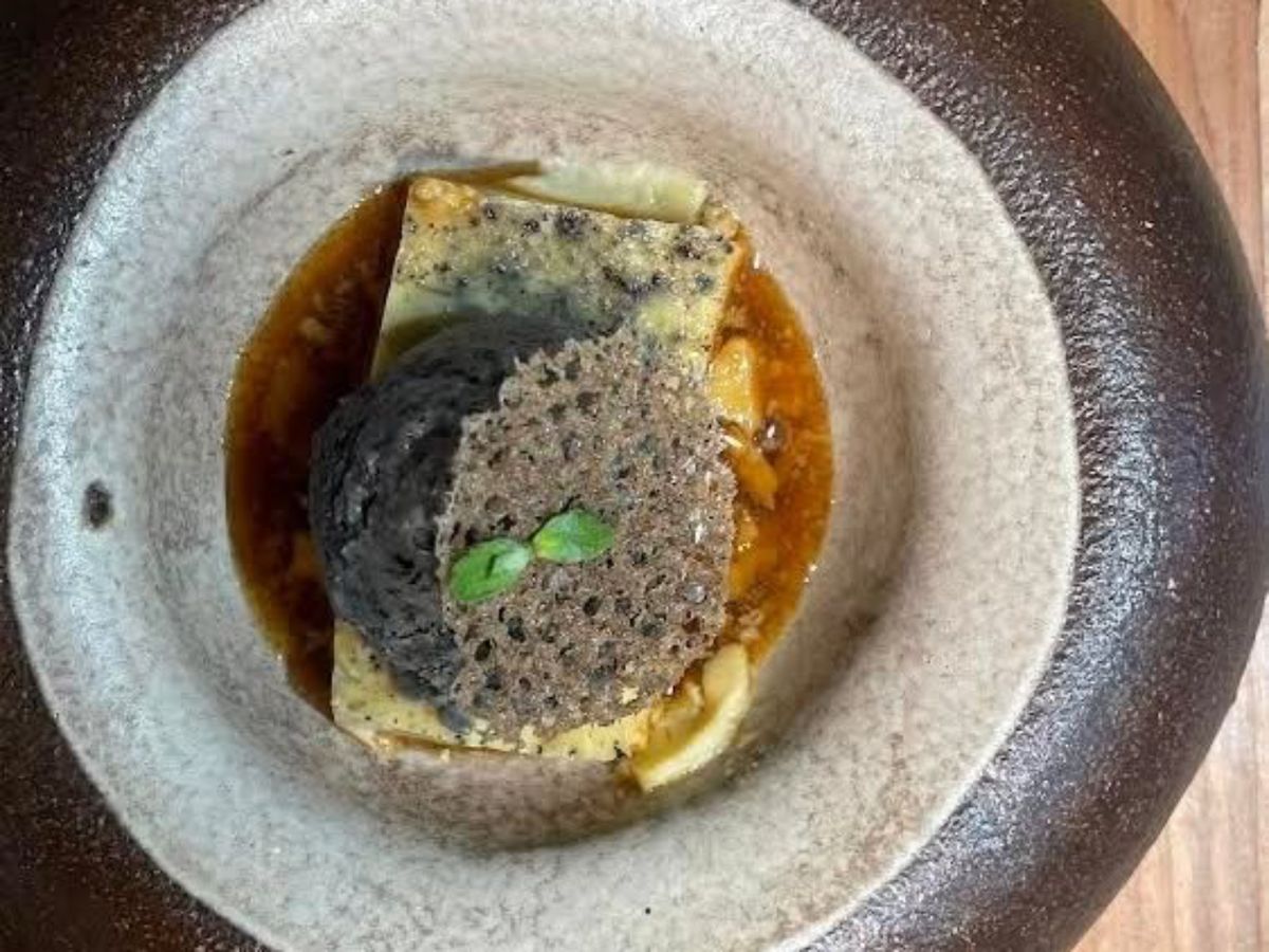Una postre de alta cocina que incorpora aceituna negra en forma de helado, con texturas crujientes y presentaciones minimalistas.