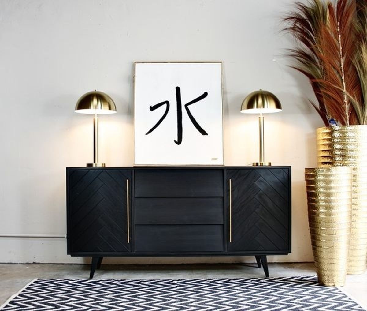 Cómoda de madera oscura decorada con complementos dorados.