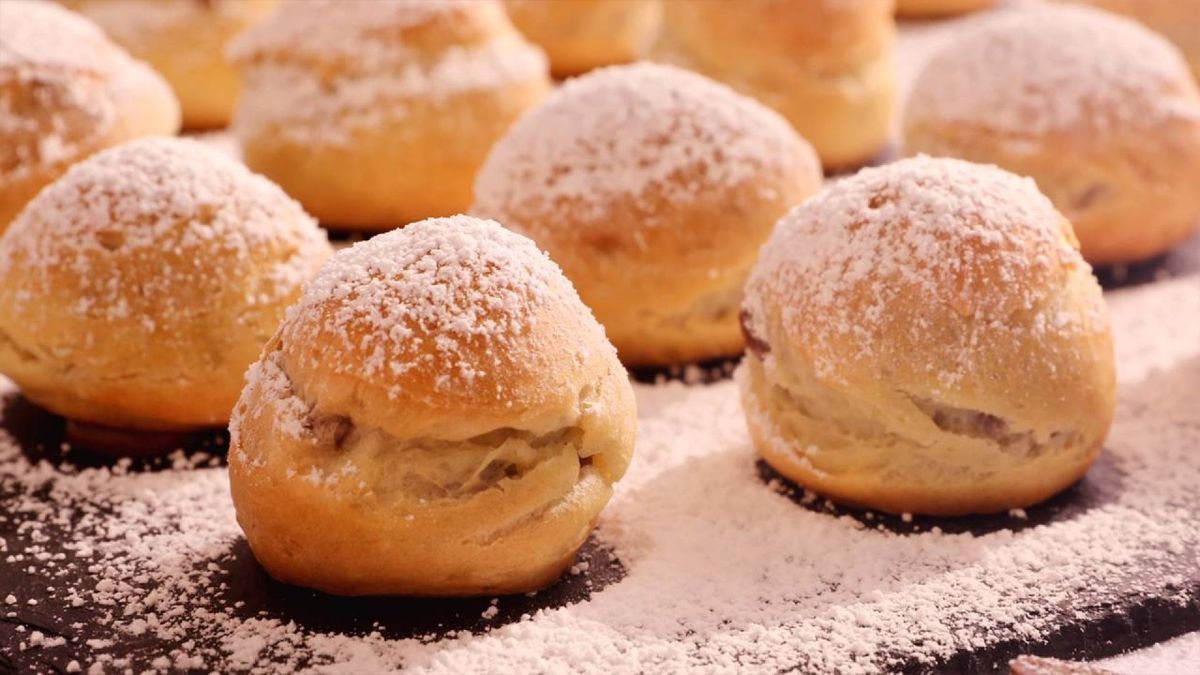 Sirve los profiteroles rellenos de crema de chocolate, decorados con un toque de azúcar glas para un acabado irresistible