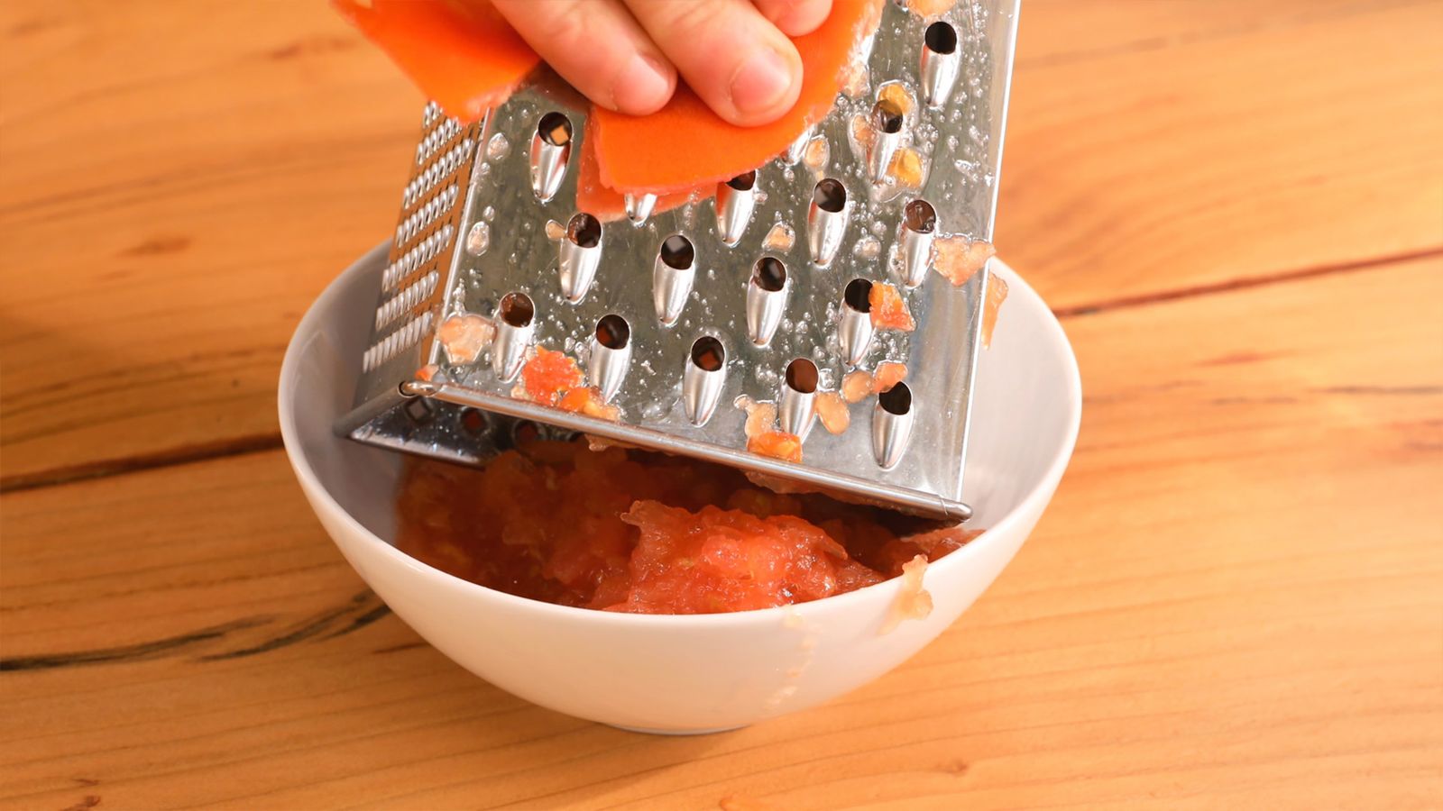 Lava y parte el tomate por la mitad, luego ralla la pulpa en un bol para incorporar su frescura Lava y parte el tomate por la mitad, luego ralla la pulpa en un bol para incorporar su frescura