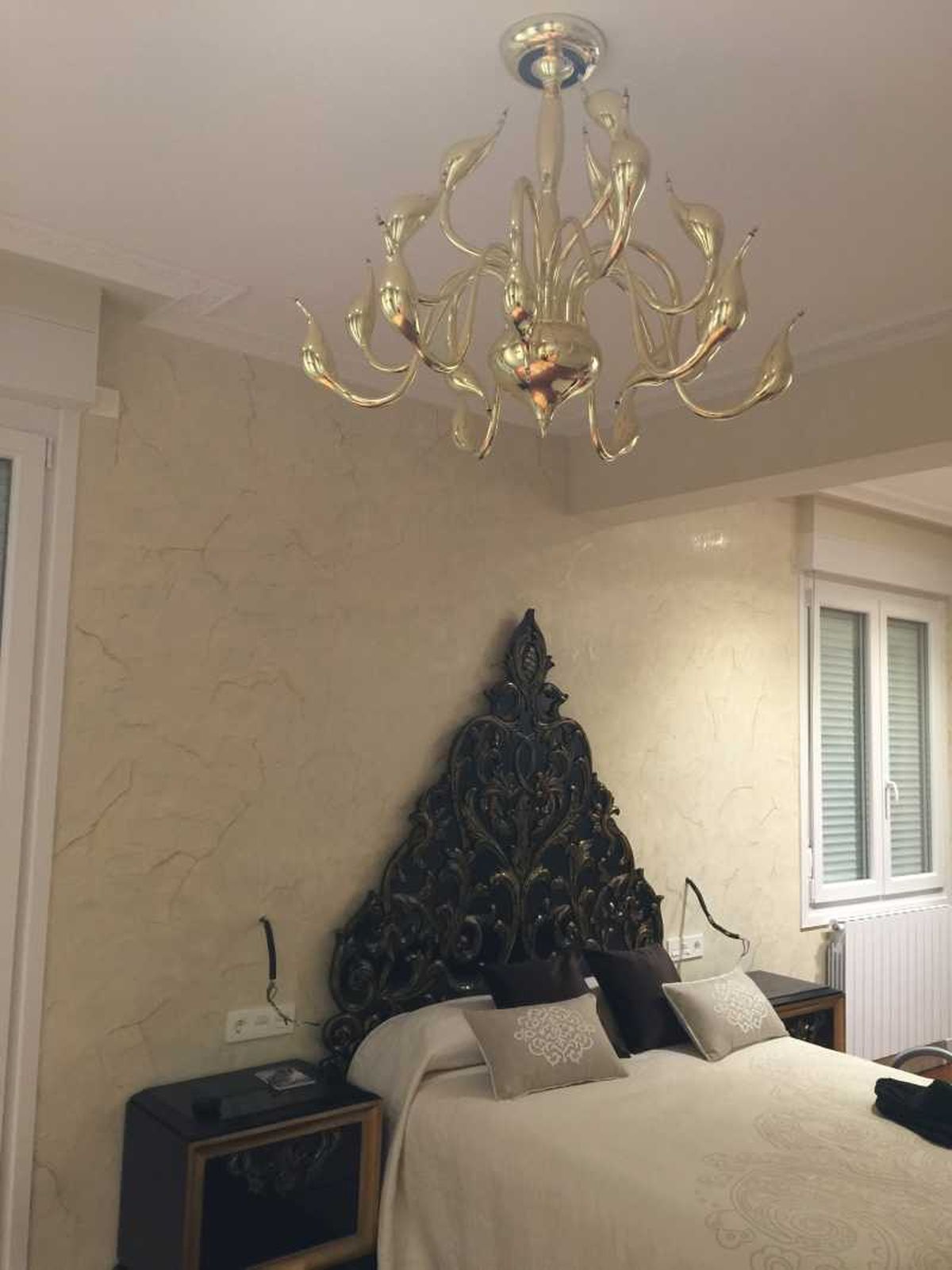 Dormitorio con cabecero de forja barroco y lámpara dorada de araña.