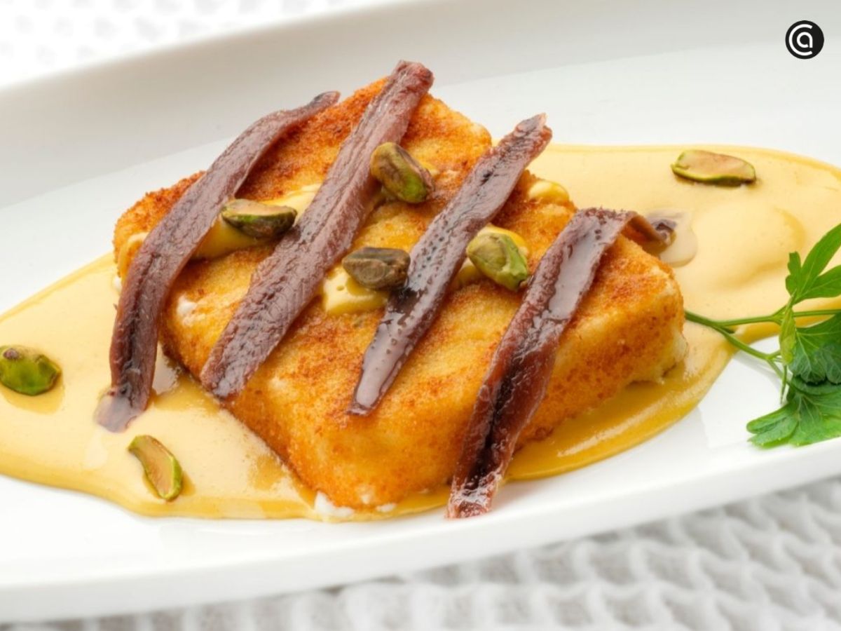 Saganaki de queso feta frito con vinagreta César, miel, pistachos y anchoas.