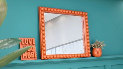 El marco terminado, decorado con medias esferas de madera y pintado en color caldera, aporta un contraste vibrante sobre la pared verde.