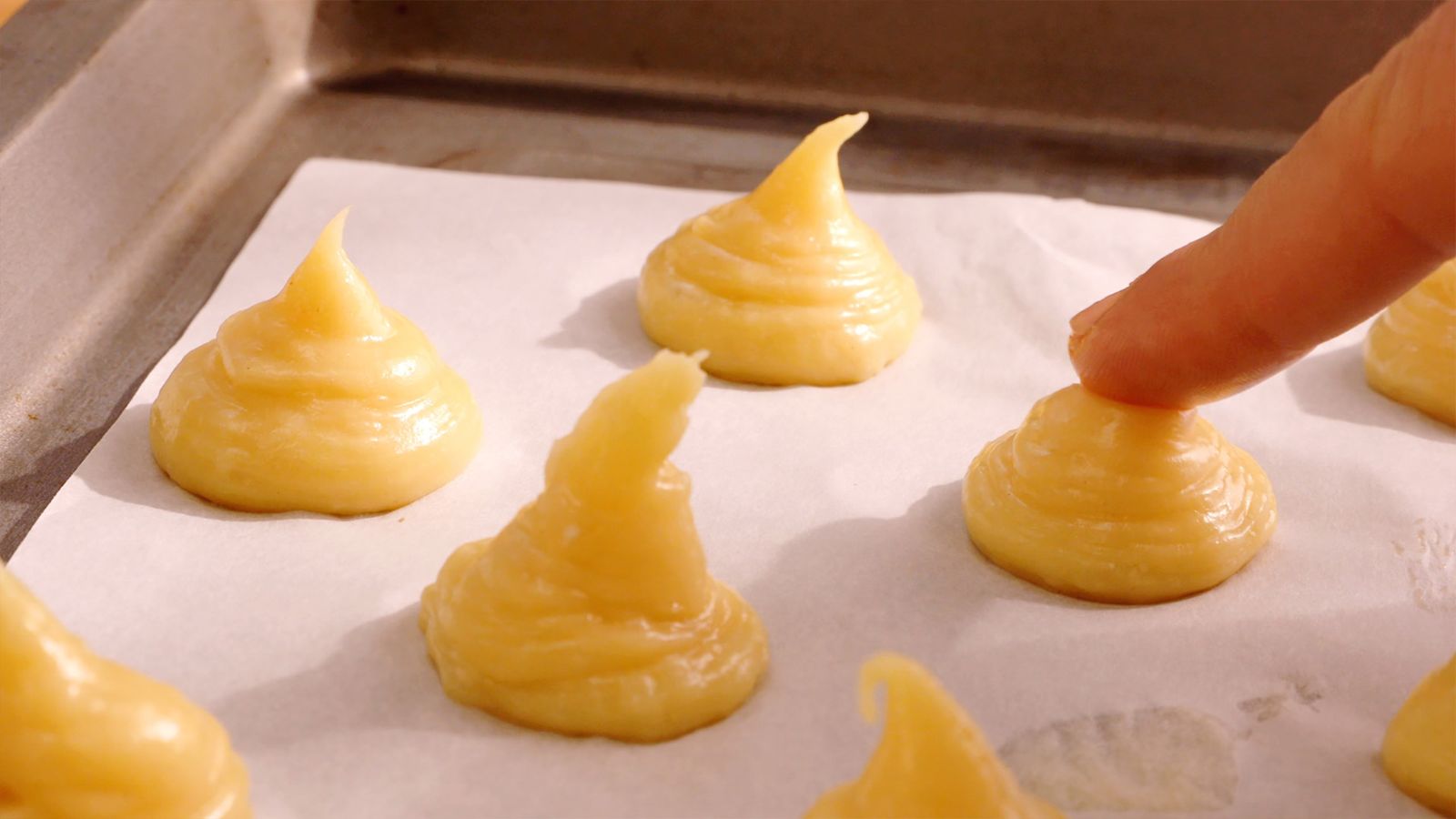 Humedece el dedo en agua y aplana ligeramente la punta de cada porción de masa para dar forma redondeada a los profiteroles