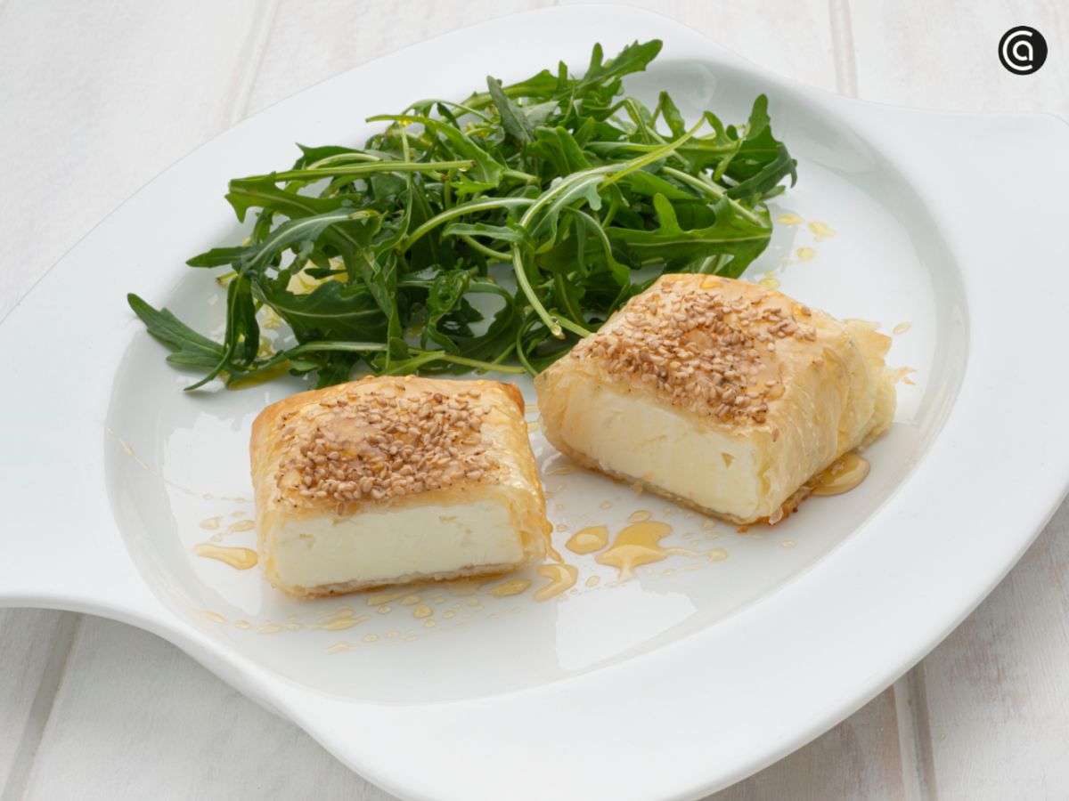 Queso feta envuelto en pasta filo con sésamo, acompañado de rúcula y un toque de miel.