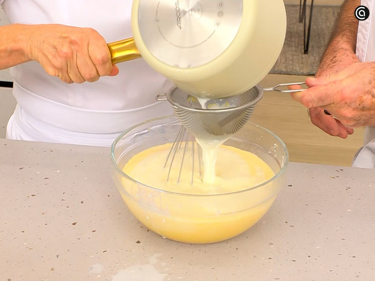 Cuela la leche infusionada sobre la mezcla de huevos y harina, y mezcla