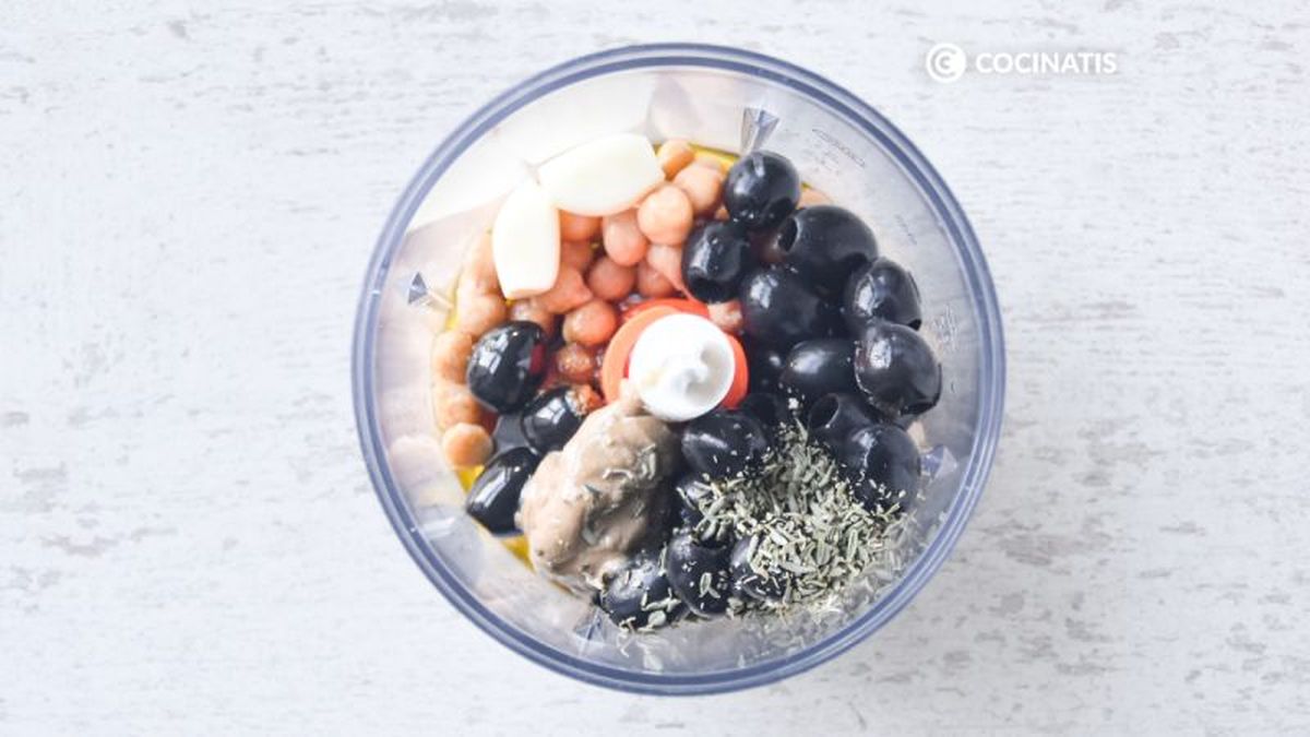 Picadora con ingredientes de hummus de aceitunas negras