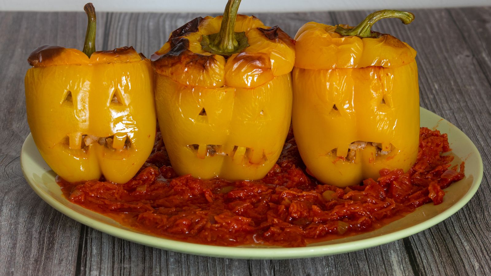 Pimientos amarillos rellenos con cara de calabaza, servidos sobre una cama de salsa de tomate