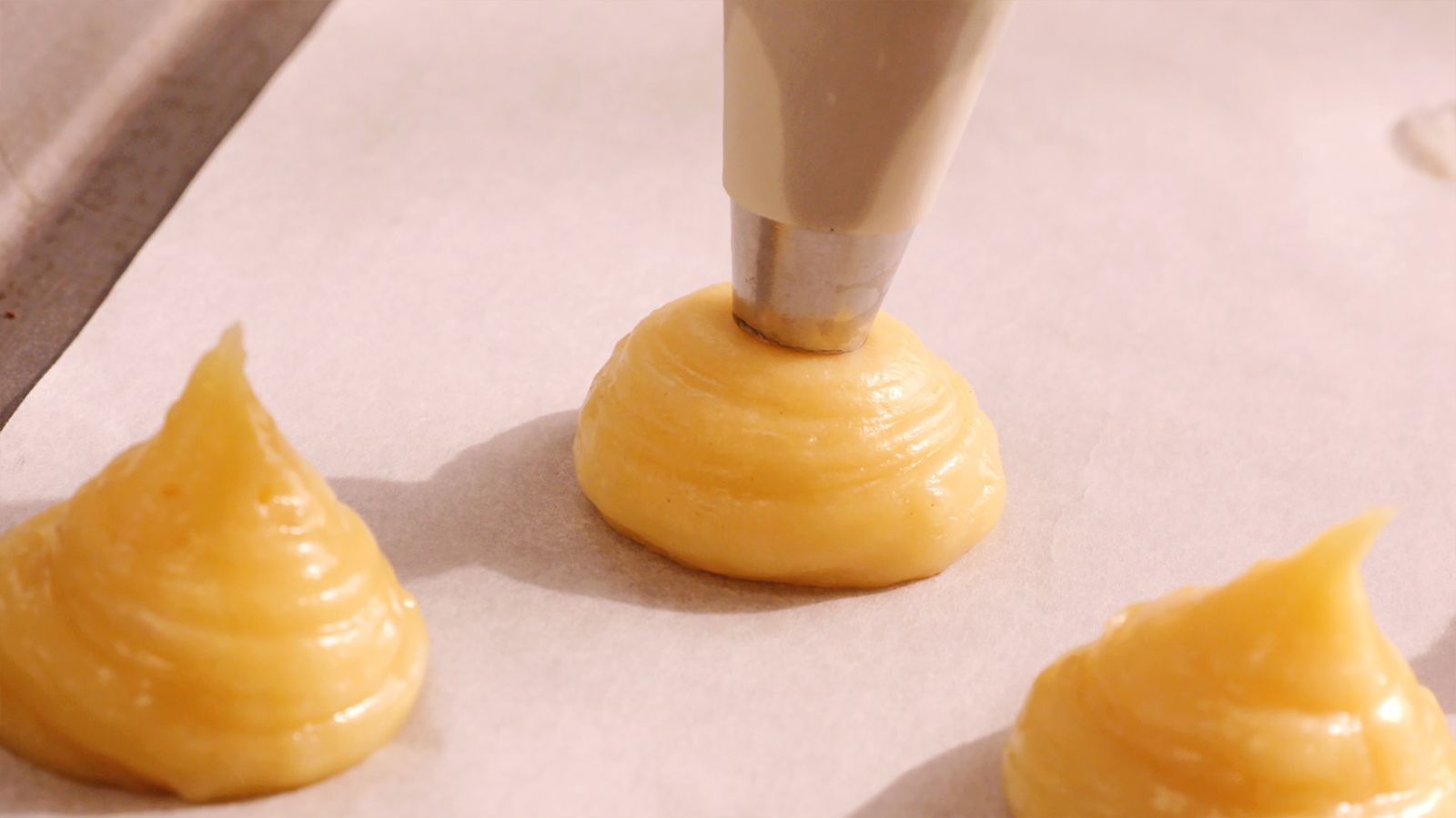 Dispón pequeñas porciones de masa de profiteroles en una bandeja con papel de horno, dejando espacio entre cada una para que se expandan al hornear