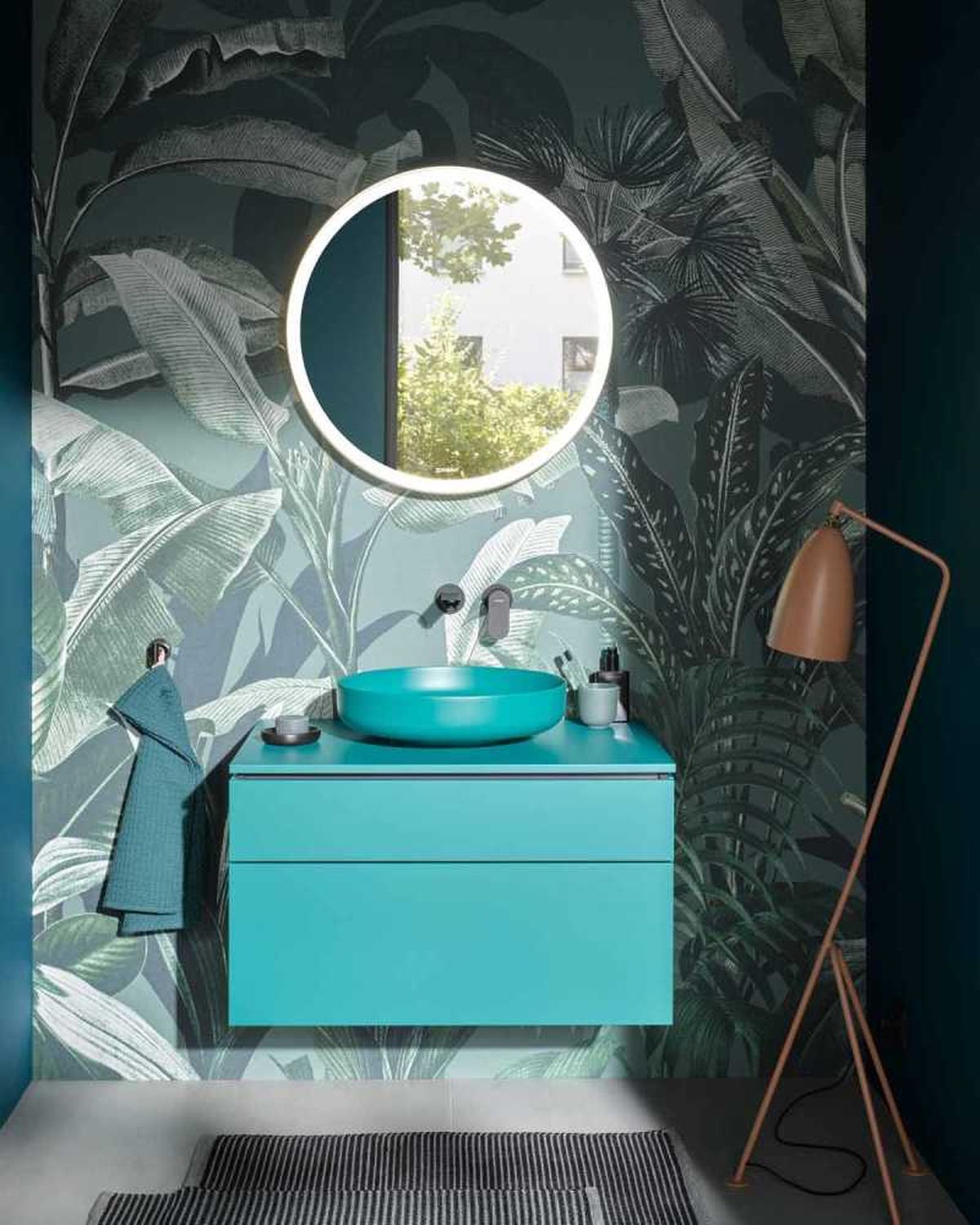 Baño con papel pintado tropical y armario y lavabo azul turquesa.