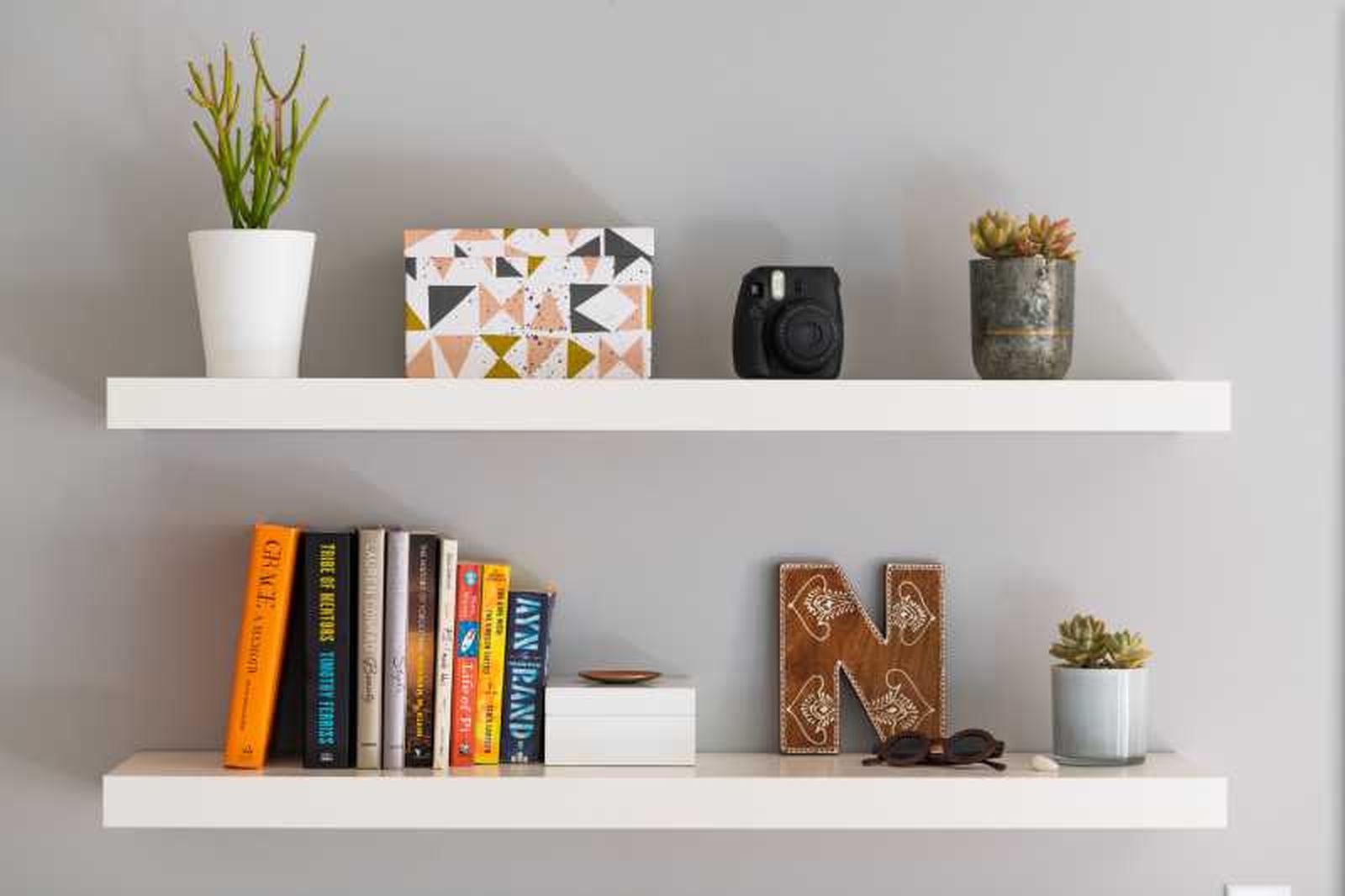 Estantería sencilla blanca con libros y complementos decorativos.
