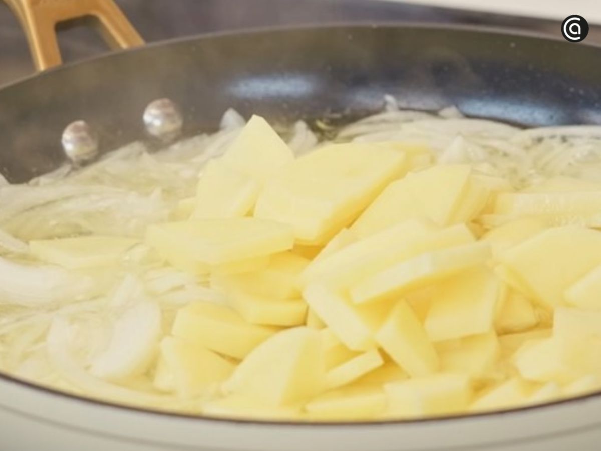 Las patatas se incorporan a la sartén junto a la cebolla para pocharse lentamente en aceite.