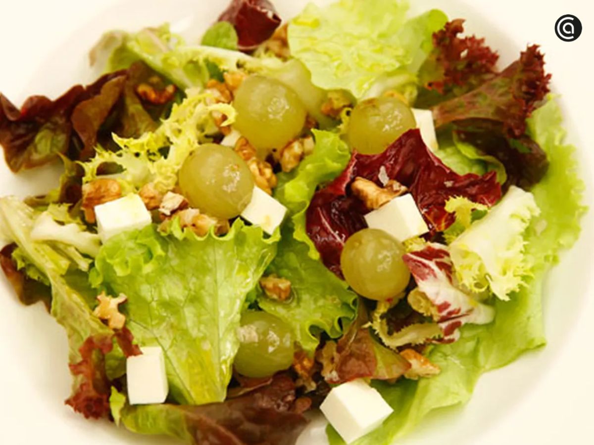 Una ensalada fresca donde las uvas y el queso se equilibran con nueces y hojas verdes.